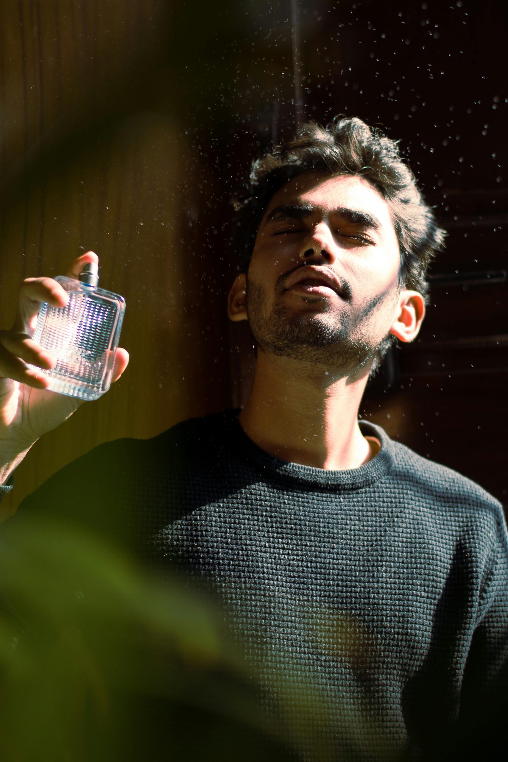 Close-up portrait of man holding a perfume bottle, basking in sunlight, eyes gently closed.